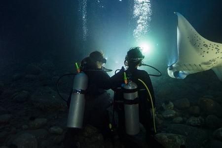 Two people in scuba gear sitting on a rock