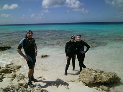 Three people in wetsuits on a beach.