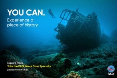 Diver exploring underwater shipwreck with PADI advertisement.