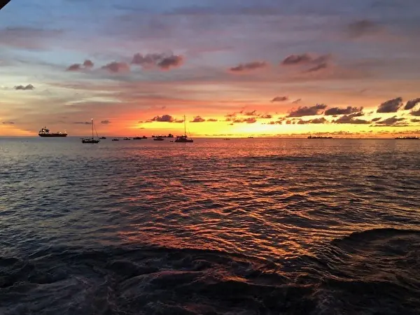 Sunset over ocean with boats in distance.
