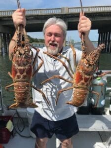 Man holding two large lobsters on boat.
