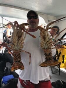 Man holding two large lobsters on boat.