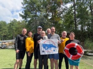 Group posing with banner and lifebuoy outdoors.