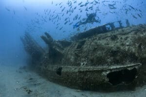Diver exploring underwater shipwreck with fish.