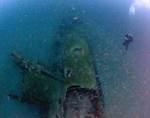 Diver exploring underwater shipwreck with fish.